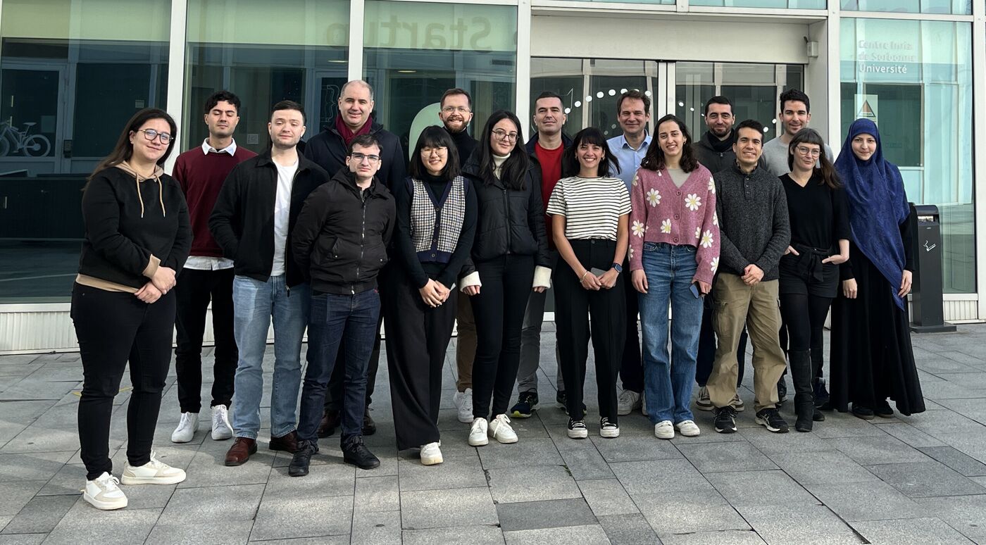 Group photo of about twenty members of the AIO team standing outside the Inria Paris building.