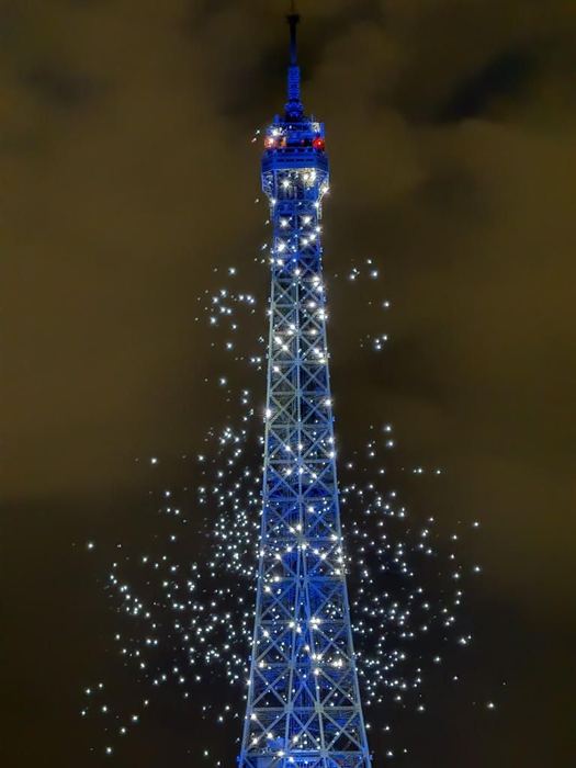 Photo of the Eiffel Tower at night surrounded by lit drones.