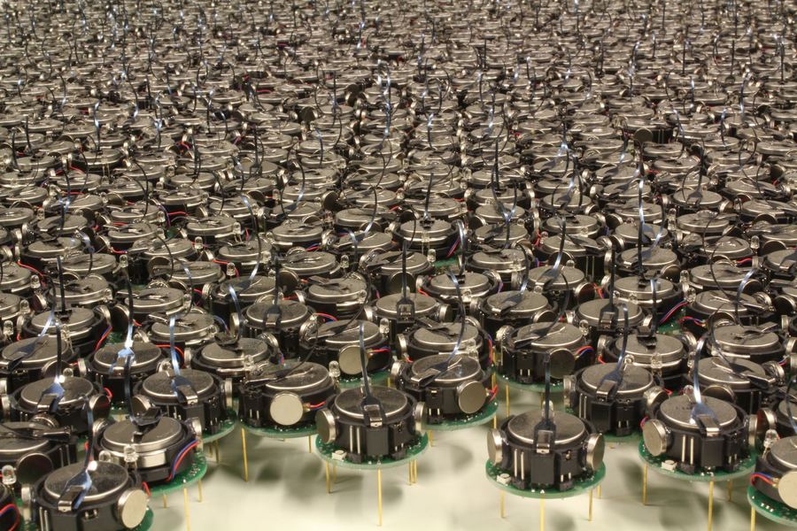 Photo of about a thousand small three-legged Kilobot robots packed on a table.